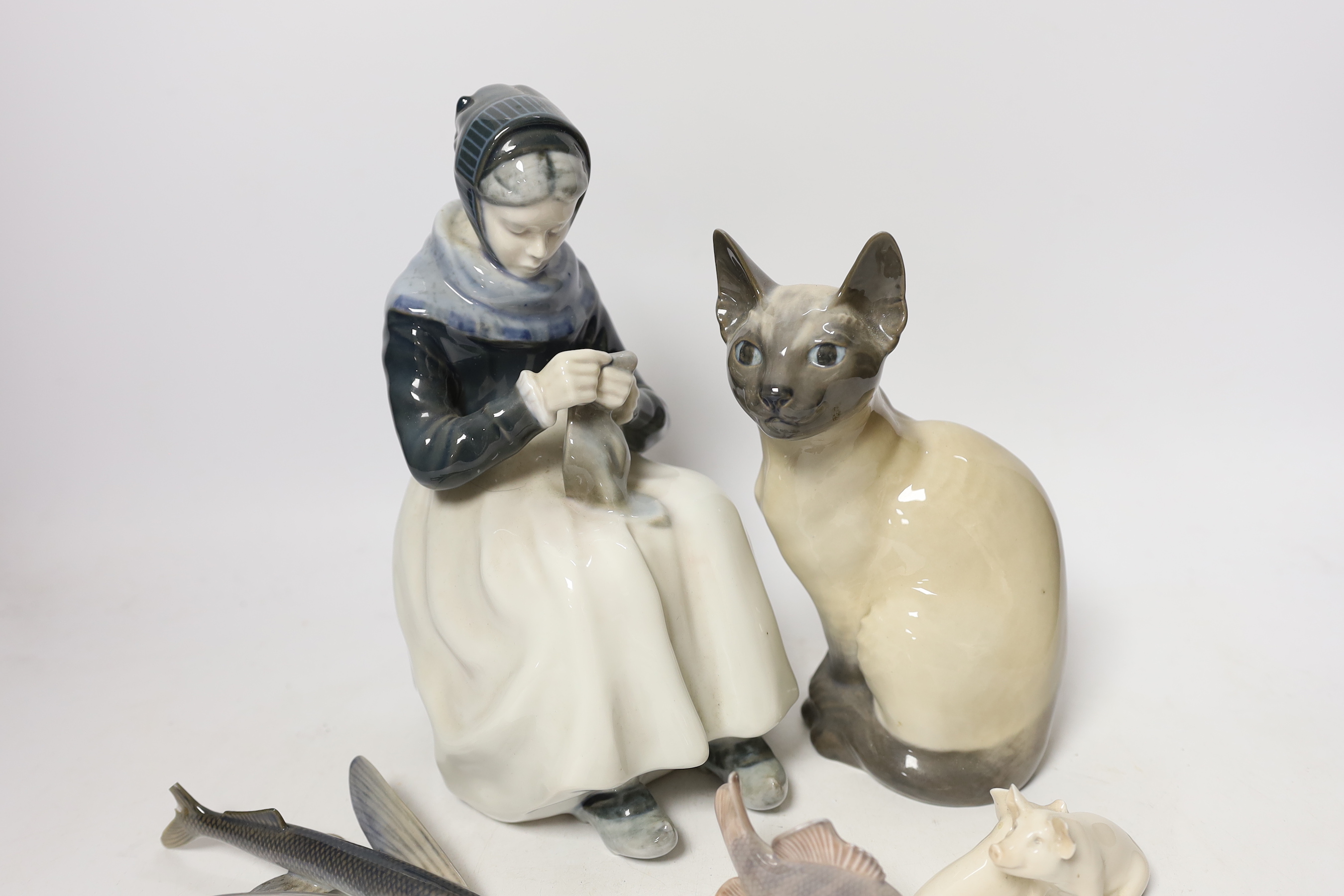 A Royal Copenhagen model of a seated lady, numbered to underside 1317, together with a further large Royal Copenhagen model of a seated Siamese cat, numbered 3281, a small group of two pigs (a.f.) numbered 1022, a seated